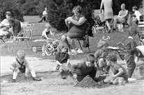 Historische Aufnahme: Sommerstimmung mit spielenden Kindern im Sandkasten und sitzenden Mütter auf Metallstühlen im Rasen